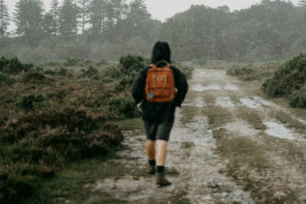 Person walking a muddy countryside path in the rain with a backpack